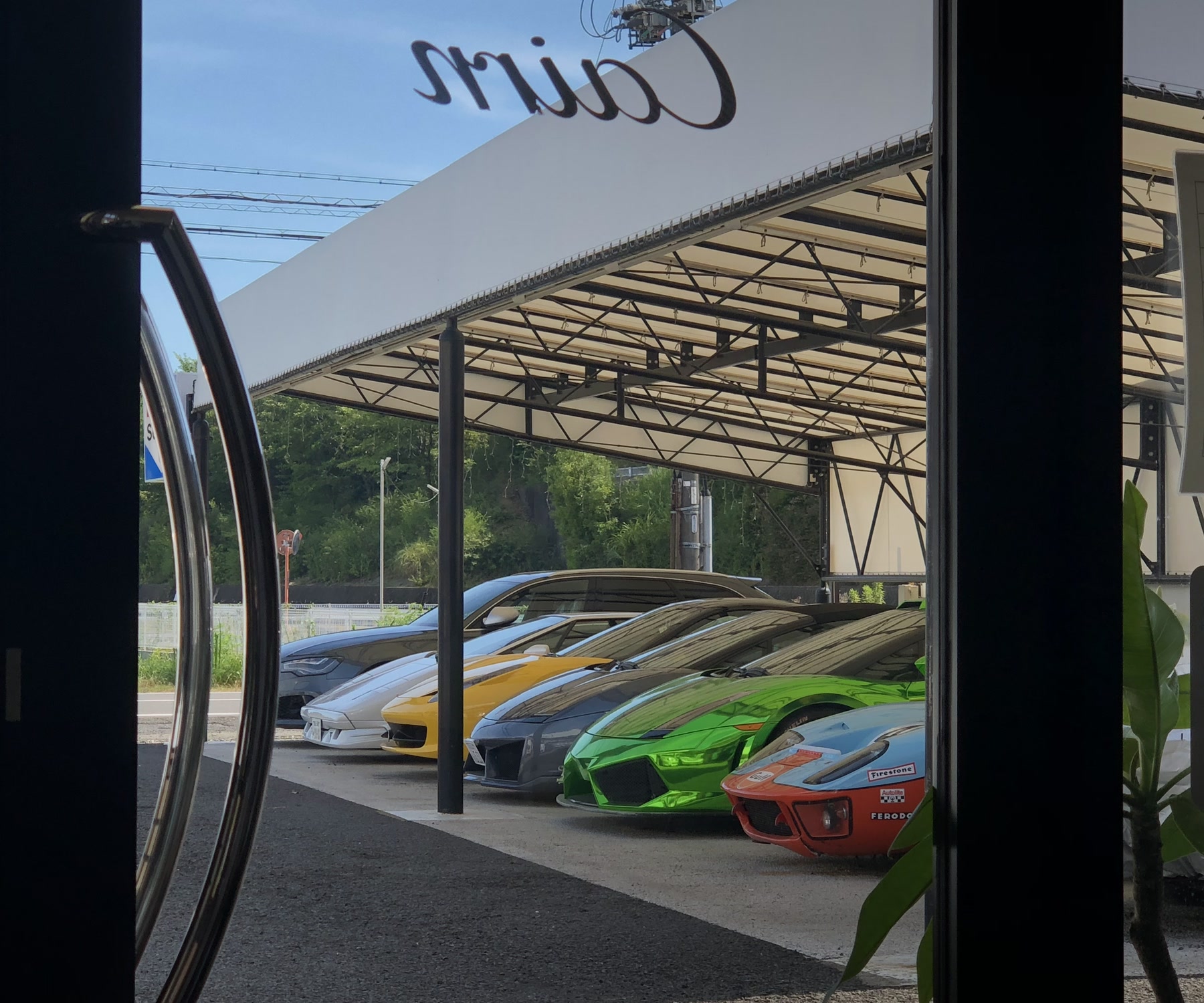 窓ガラスのCairnロゴ越しに並ぶスーパーカー